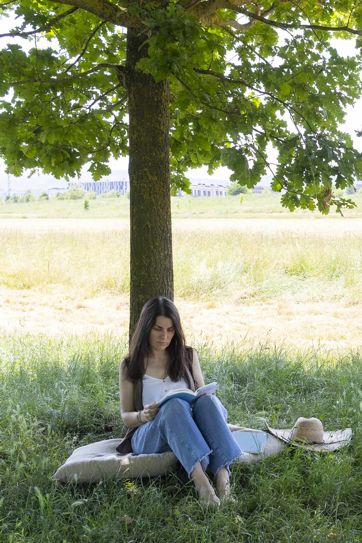 Esther Mambrilla leyendo sentada bajo un árbol en un prado de Vitoria-Gasteiz